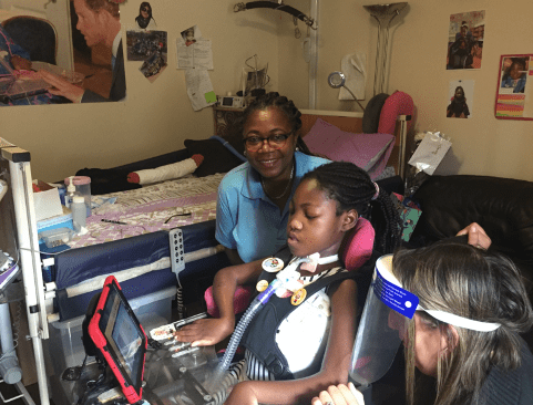 Young girl in wheelchair with ventilator and support and medical staff working on an iPad